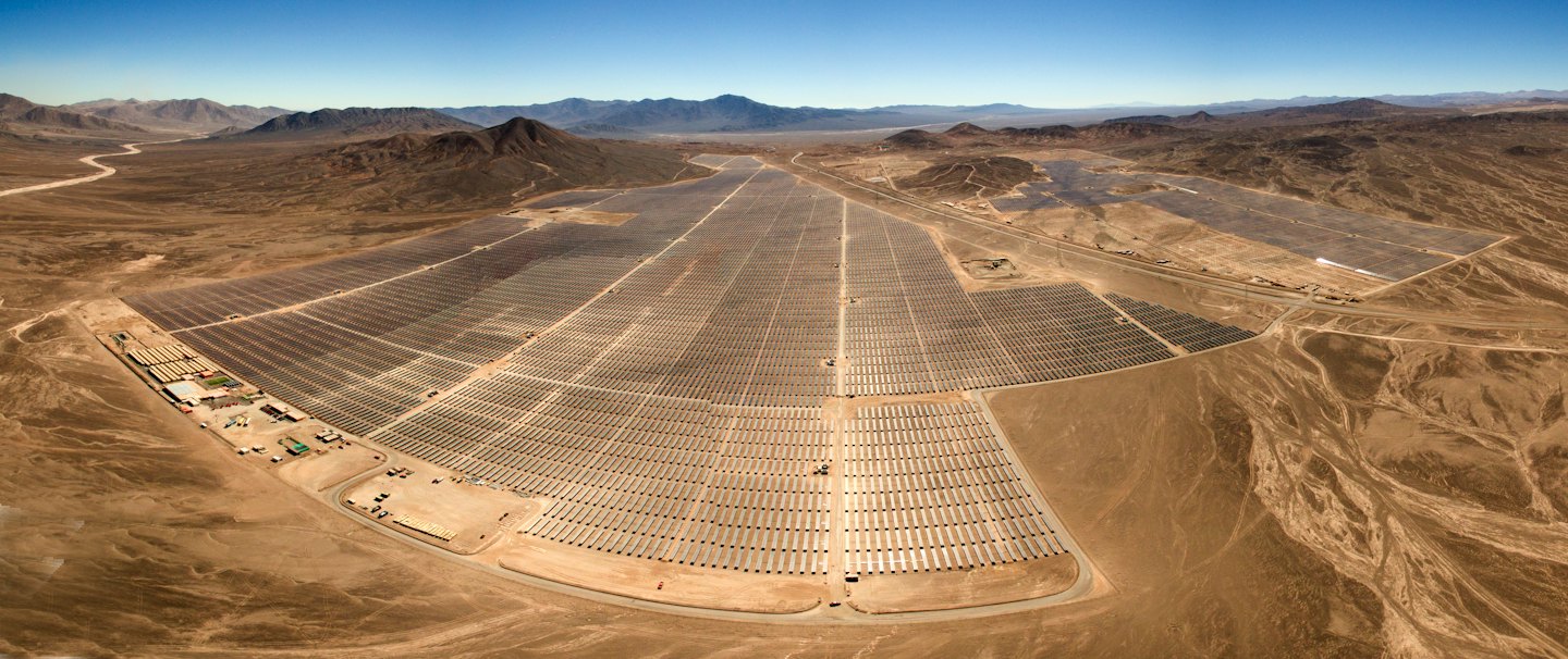 Miles de paneles solares cubren un paisaje desértico bajo un cielo azul.